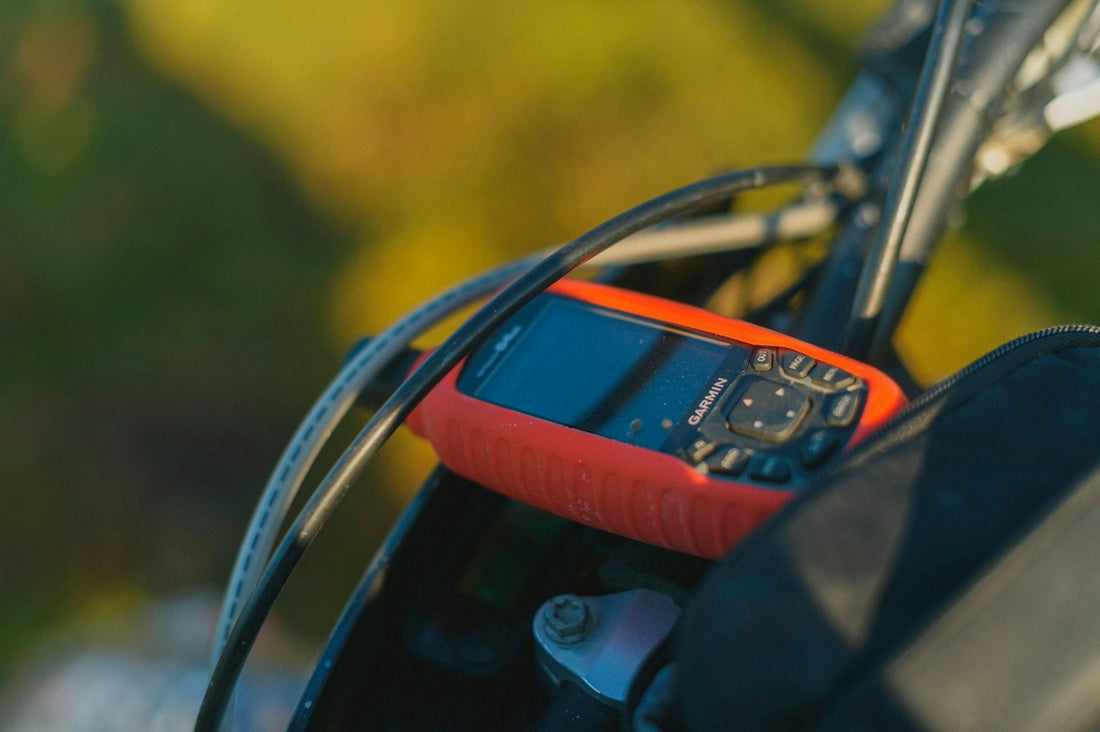 A red GPS device mounted on bicycle handlebars in warm golden hour light